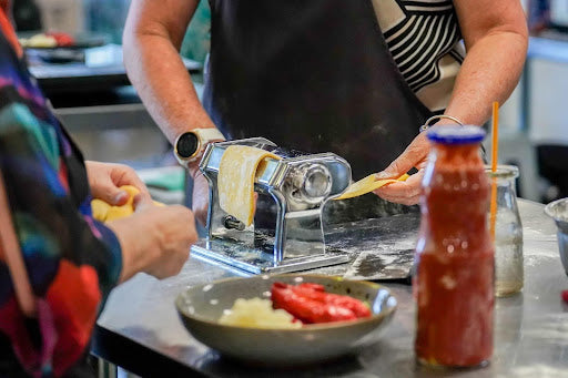 Professional chef making fresh pasta using a pasta machine in a kitchen workspace