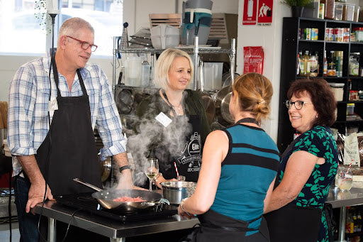 Group of smiling adults in aprons cooking stir-fry with wok during 2026 cooking class, ultimate experience gift voucher idea.